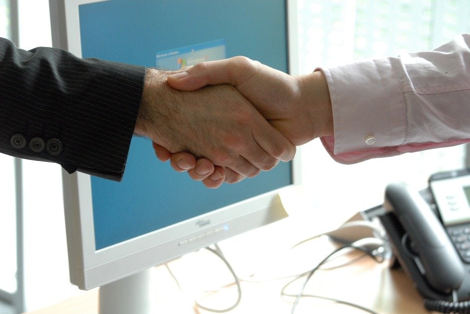 Shaking hands in front of computer screen